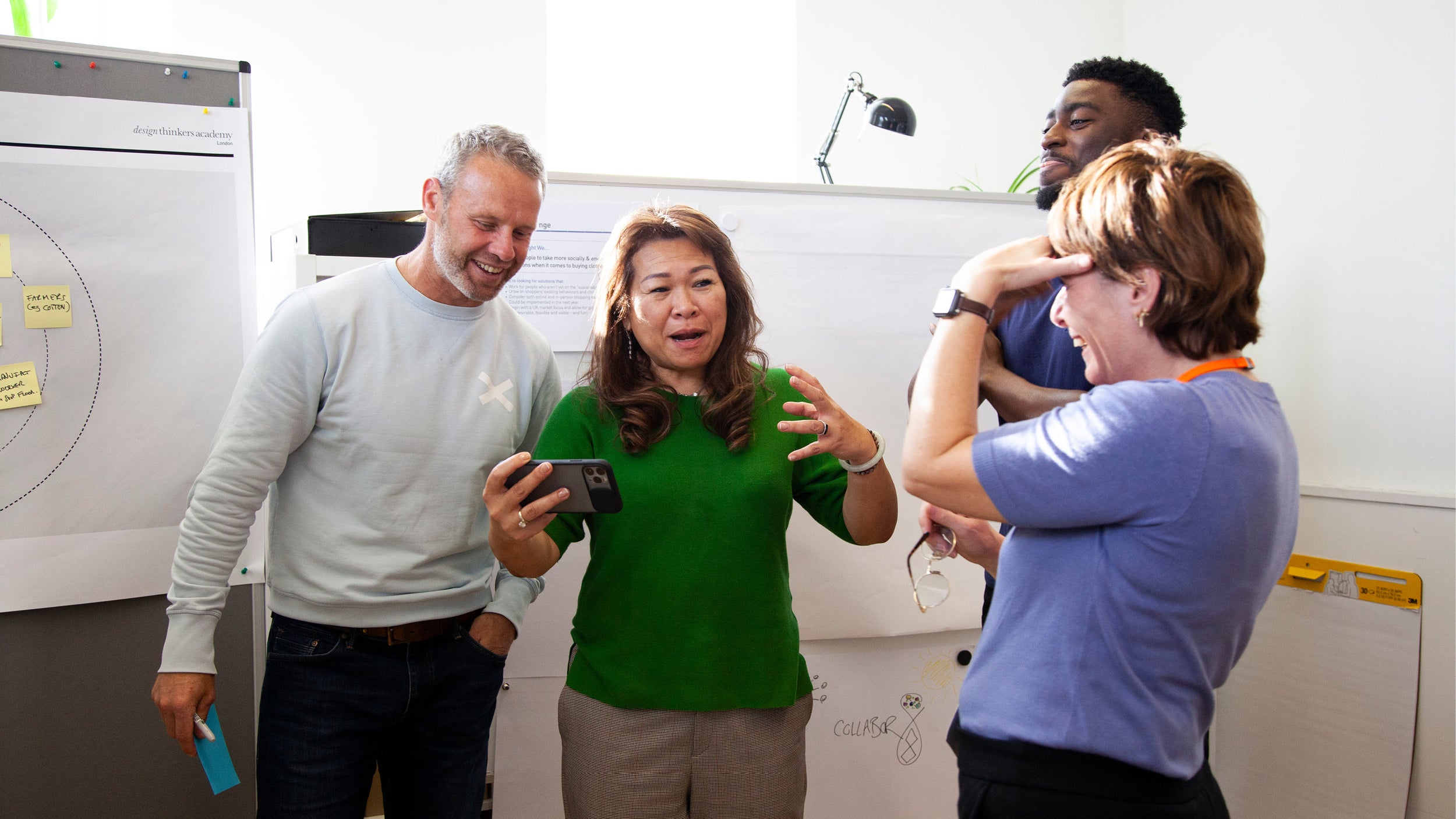 A group of people at one of our courses, gathered around a phone looking at a prototype and laughing